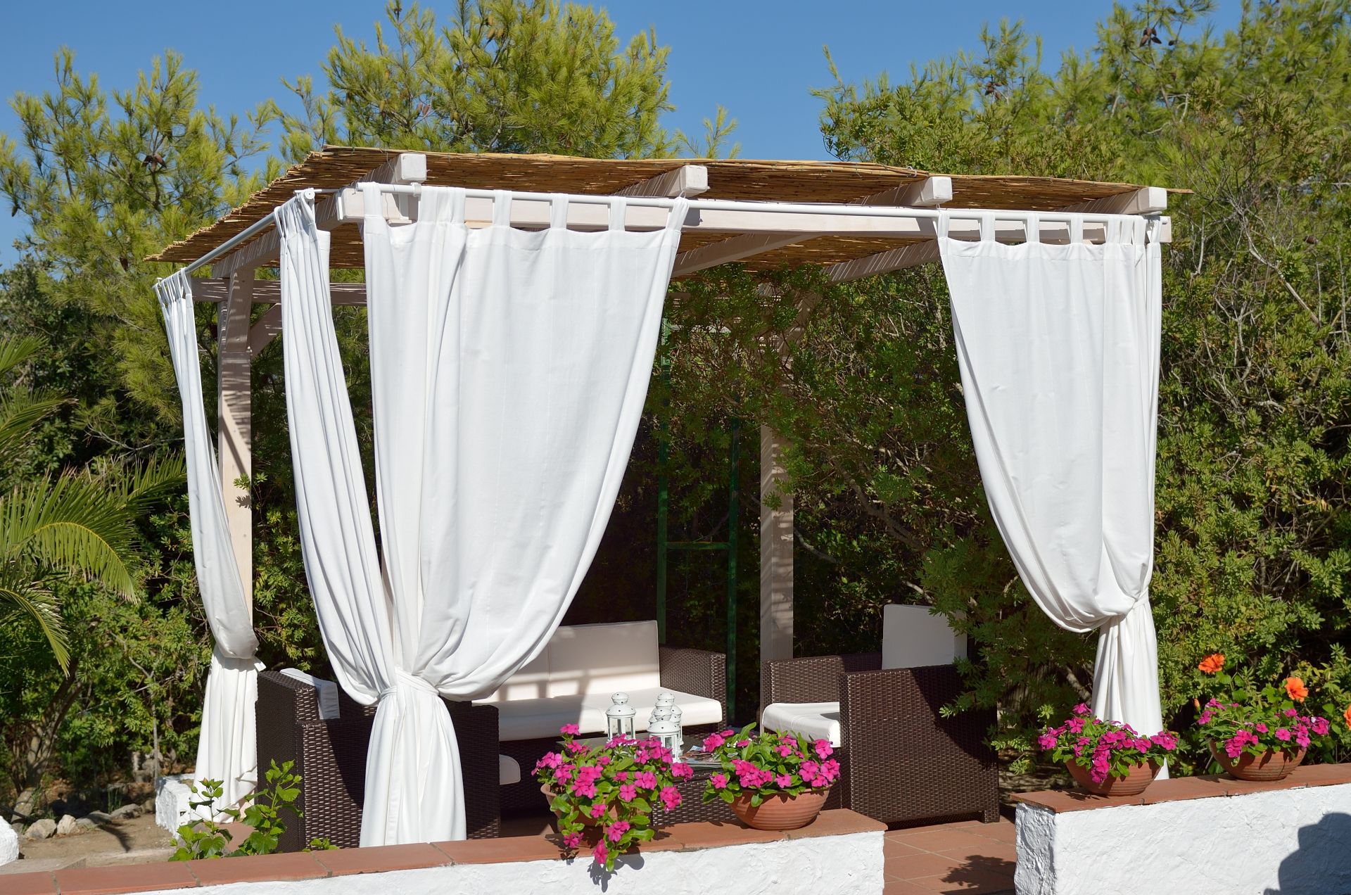 Offener Lounge-Pavillon mit weißen Vorhaengen und gemuetlichen Sitzmoebeln im mediterranen Garten